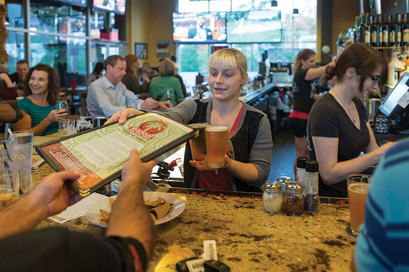 Donna Lucksavage juggles a menu and a couple of beers behind the bar at Ruckus as Joanie Koontz, right, works the register. 