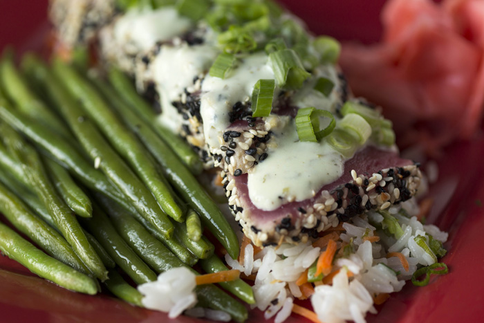 Sesame encrusted ahi tuna is served with jasmine rice and a vegetable. It is finished with cilantro wasabi cream sauce.