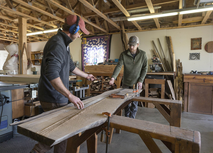 Quinn Ferebee, left, and Doug Boytos of Live Edge Wood Designs get ready to trim a slab that will become a dining room table. The pair works with the tree’s natural shape in their designs. “The slabs dictate what can be made from them,” says Boytos.